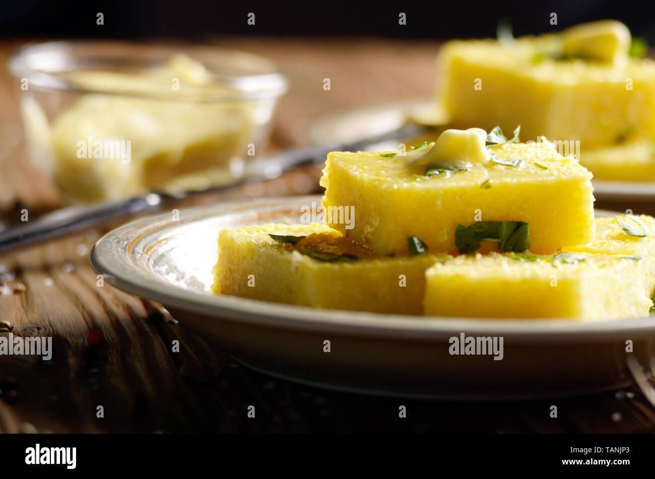 La polenta avec du beurre et les verts sur un plat d'argile sur table rustique en bois Banque D'Images