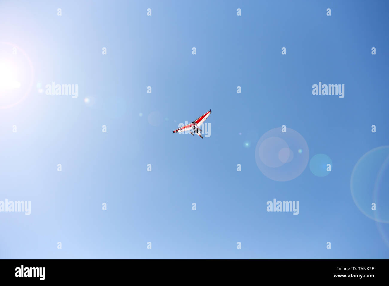 Blanc-rouge deltaplane motorisé dans le ciel bleu, avec l'éblouissement causé par le soleil. Banque D'Images