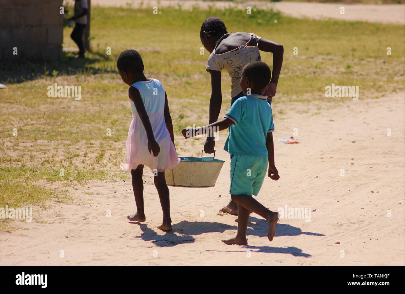 Les jeunes enfants africains transportent l'eau du village d'un robinet d'eau retour à l'accueil pour faire leur lavage. Banque D'Images