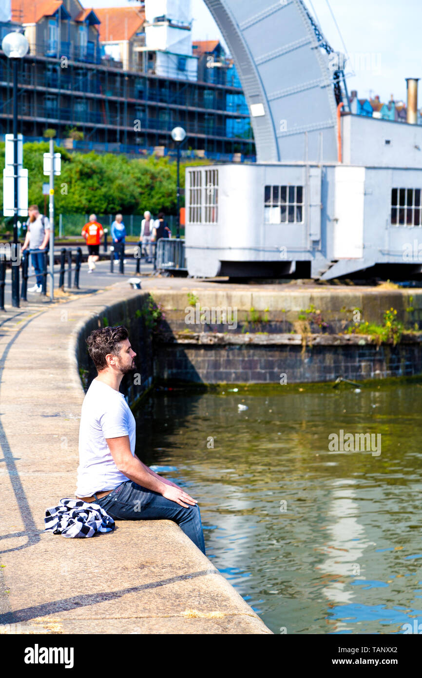 L'homme aux yeux clos et les paumes sur ses genoux en méditant au Bristol Harbourside, Princes Wharf, UK Banque D'Images