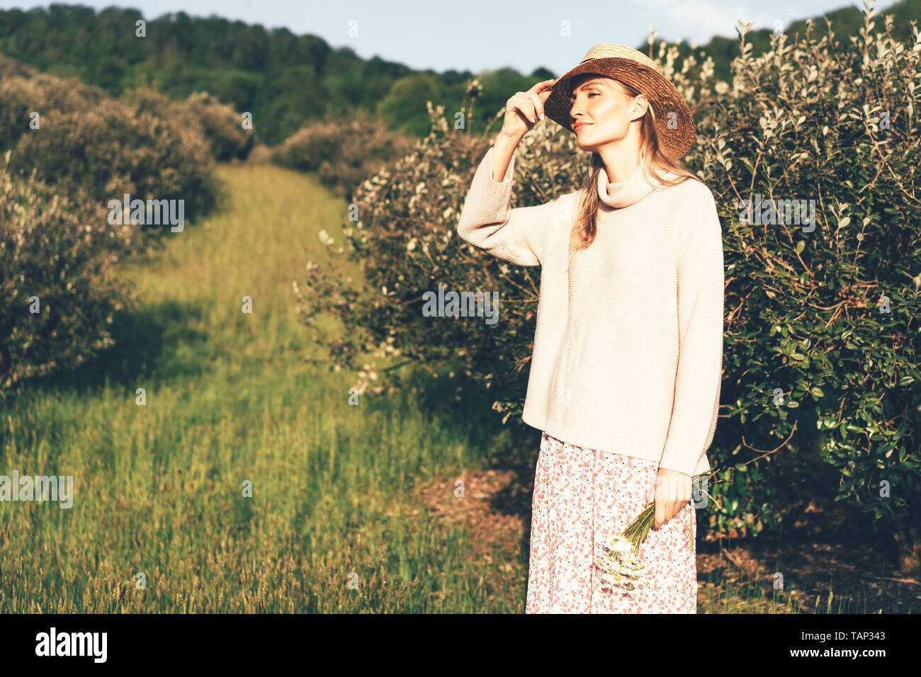 Cute blonde girl dans un style provençal et chapeau de paille, promenade dans le jardin verdoyant, le concept de bonheur et l'insouciance Banque D'Images