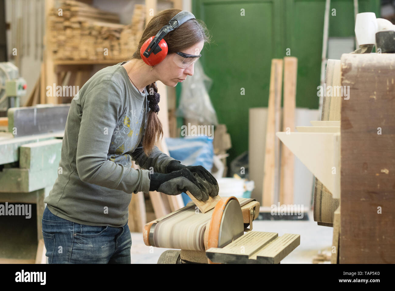 Jeune femme à l'aide d'une ponceuse de ceinture de sable de planche en bois à l'atelier Banque D'Images