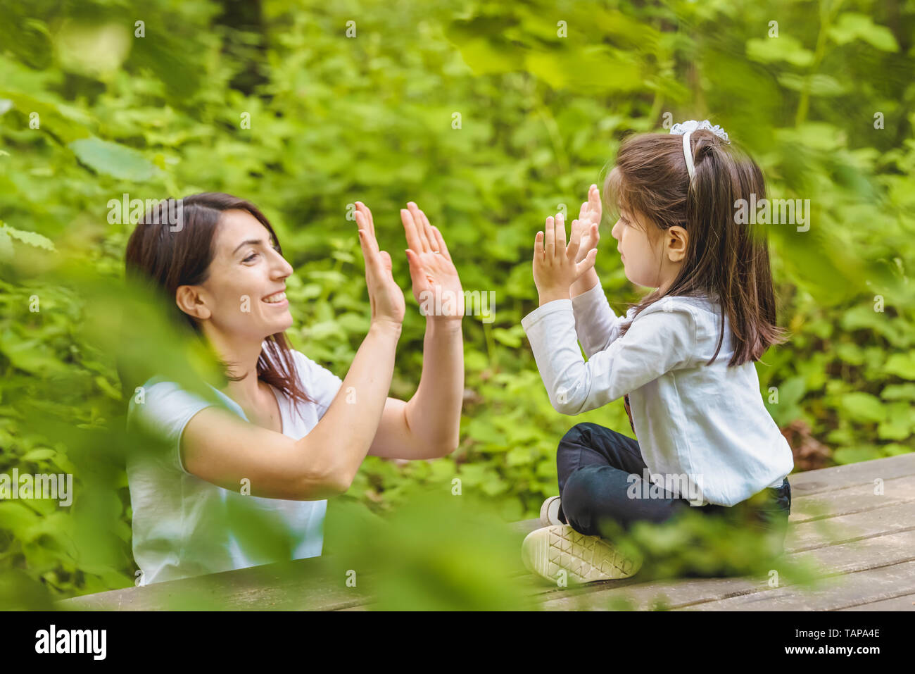 Jeune maman et sa petite fille s'amuser ensemble sur banc en bois en forêt.Happy mother and daughter moments avec amour et émotion naturelle Banque D'Images