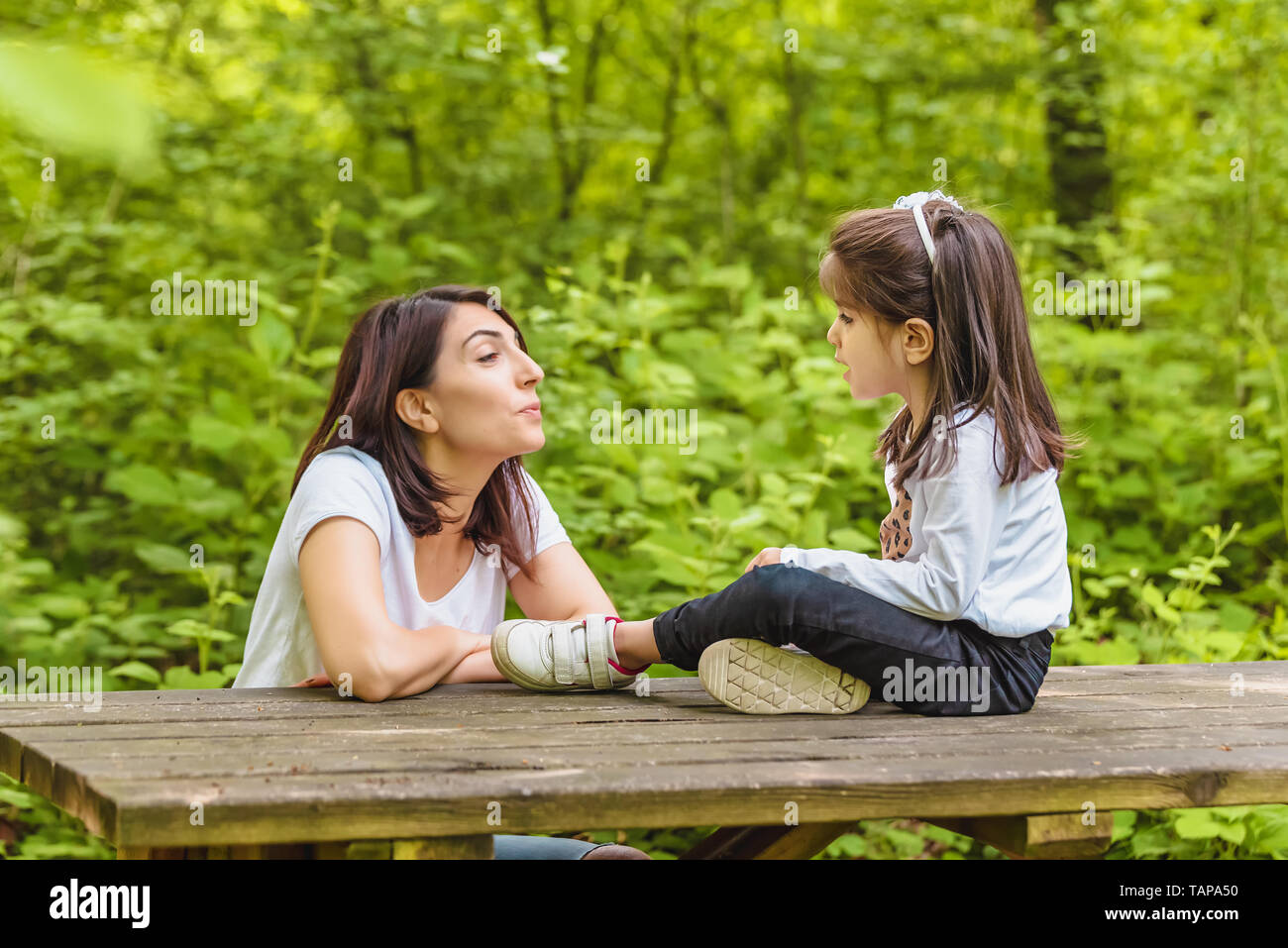 Jeune maman et sa petite fille s'amuser ensemble sur banc en bois en forêt.Happy mother and daughter moments avec amour et émotion naturelle Banque D'Images