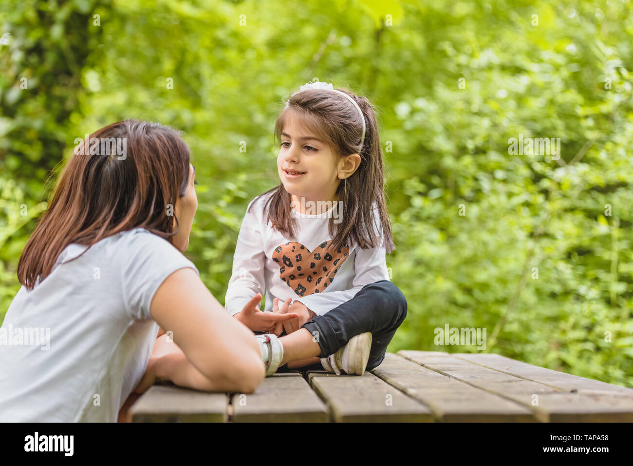 Jeune maman et sa petite fille s'amuser ensemble sur banc en bois en forêt.Happy mother and daughter moments avec amour et émotion naturelle Banque D'Images