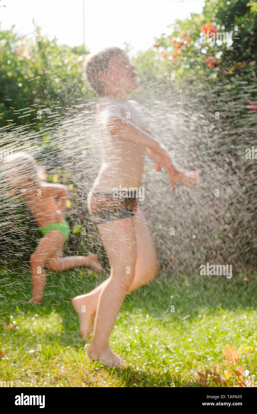 Heureux les enfants s'amusant palying sprinkleur avec pelouse dans un jardin d'été - vacances d'concept Banque D'Images