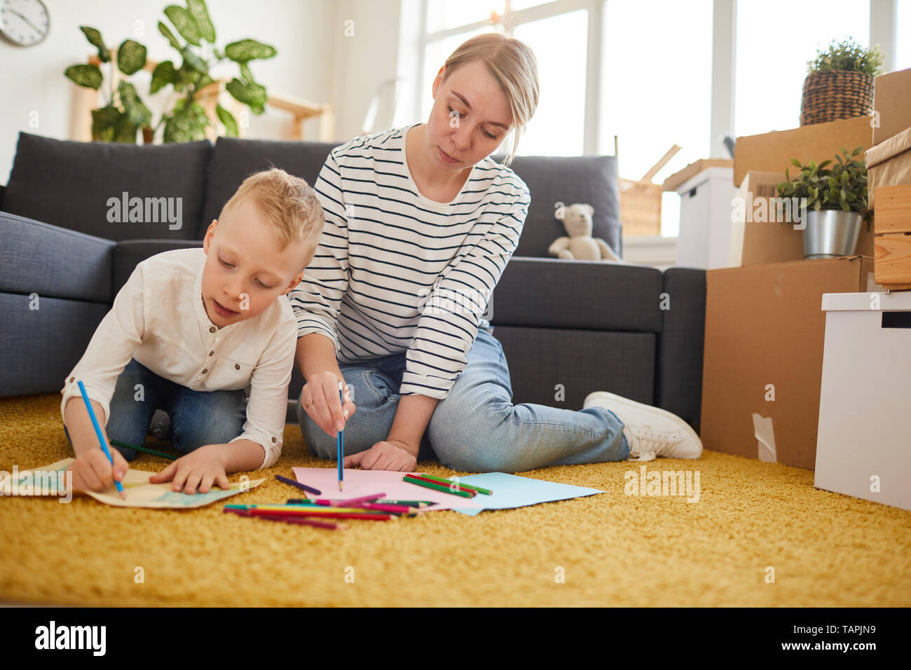 Serious attractive la mère et son fils assis sur un tapis de création dans la salle de séjour avec des cartons et réunir les Banque D'Images