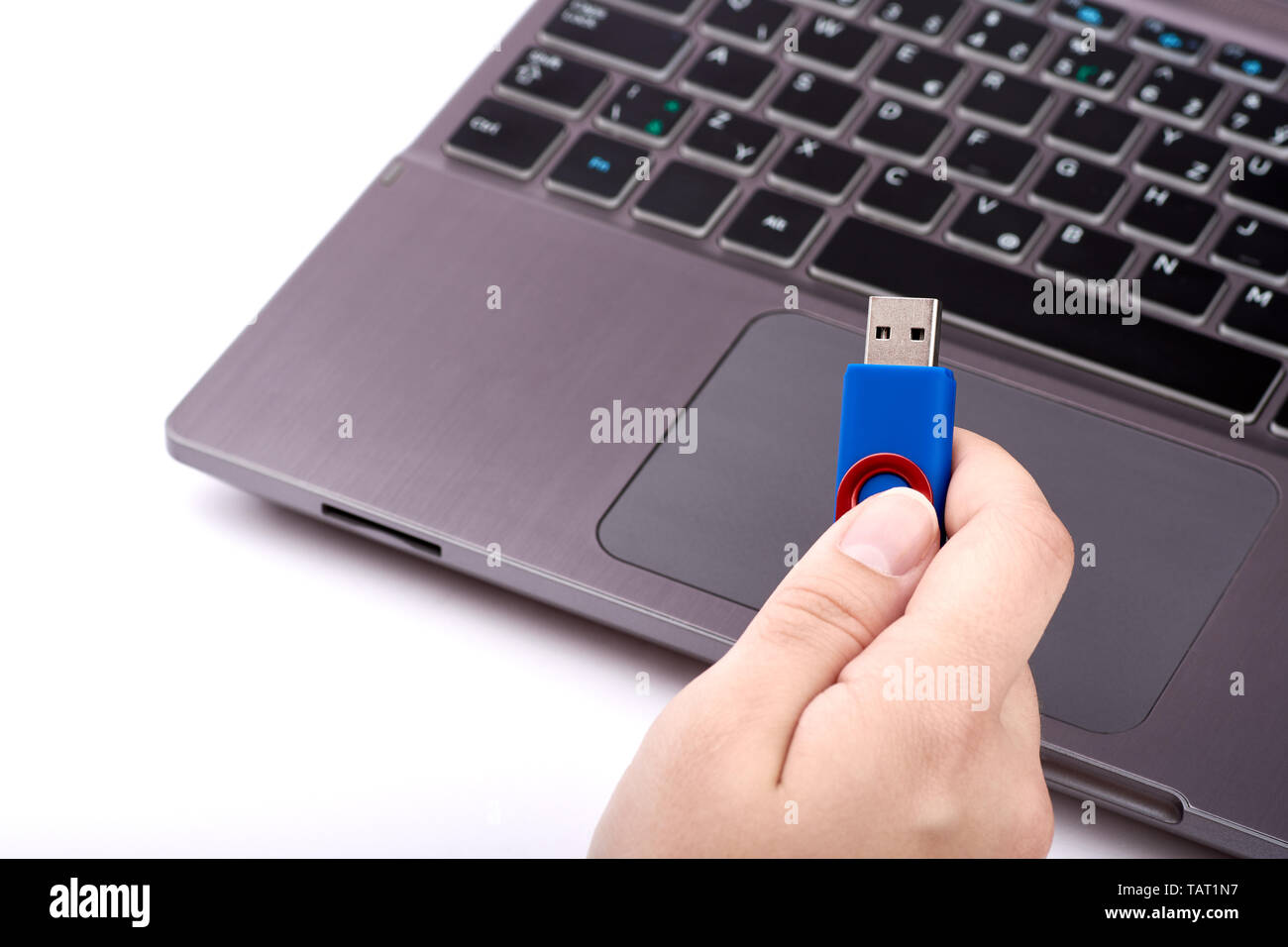 Une femme est titulaire d'un lecteur flash USB bleu dans sa main. Ordinateur portable avec clavier d'argent noir sur fond flou - Isolé sur fond blanc. Banque D'Images