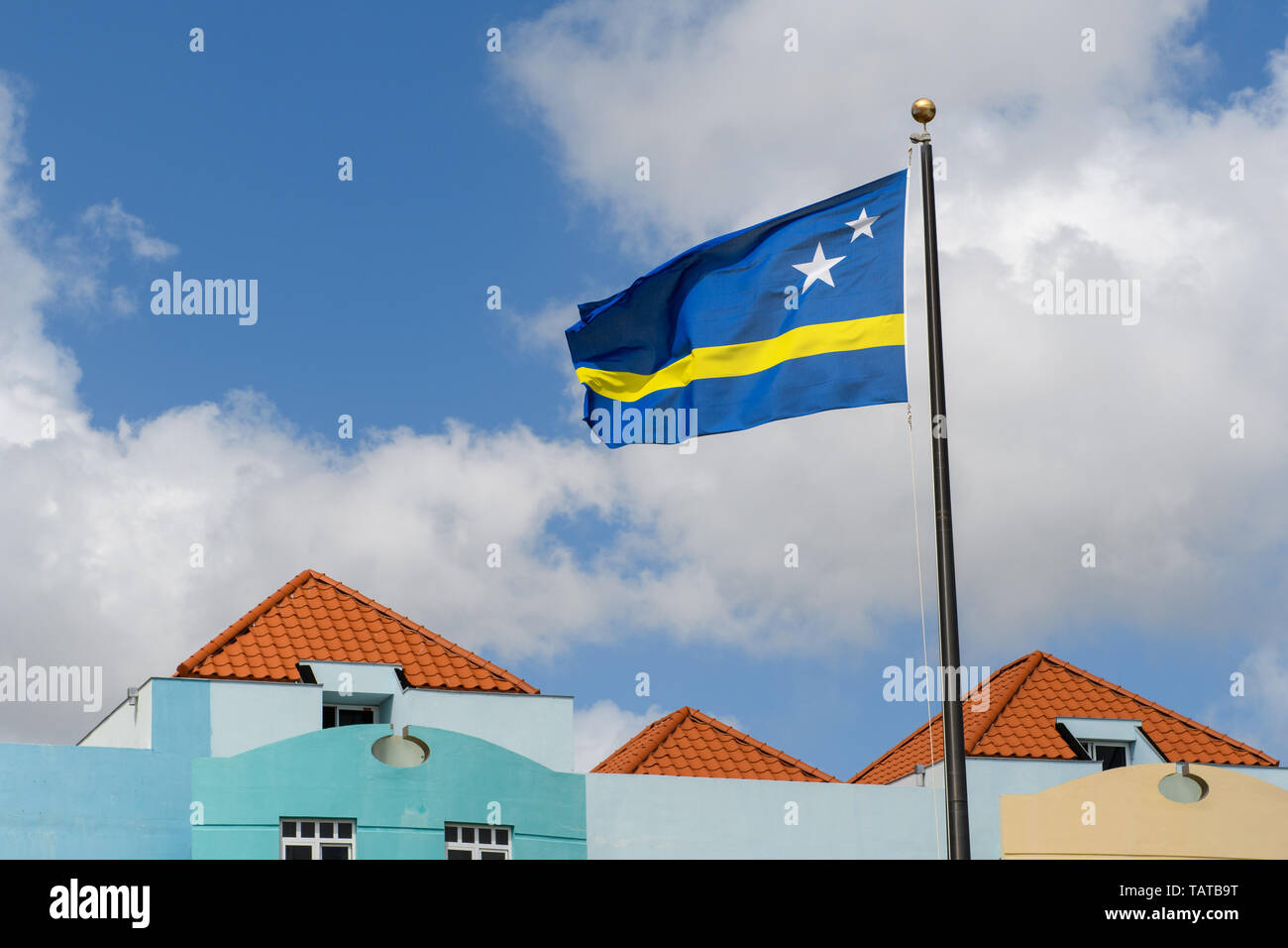 Le drapeau bleu-jaune s'agite dans le bleu ciel nuageux au-dessus des toits et des murs bleus. Banque D'Images