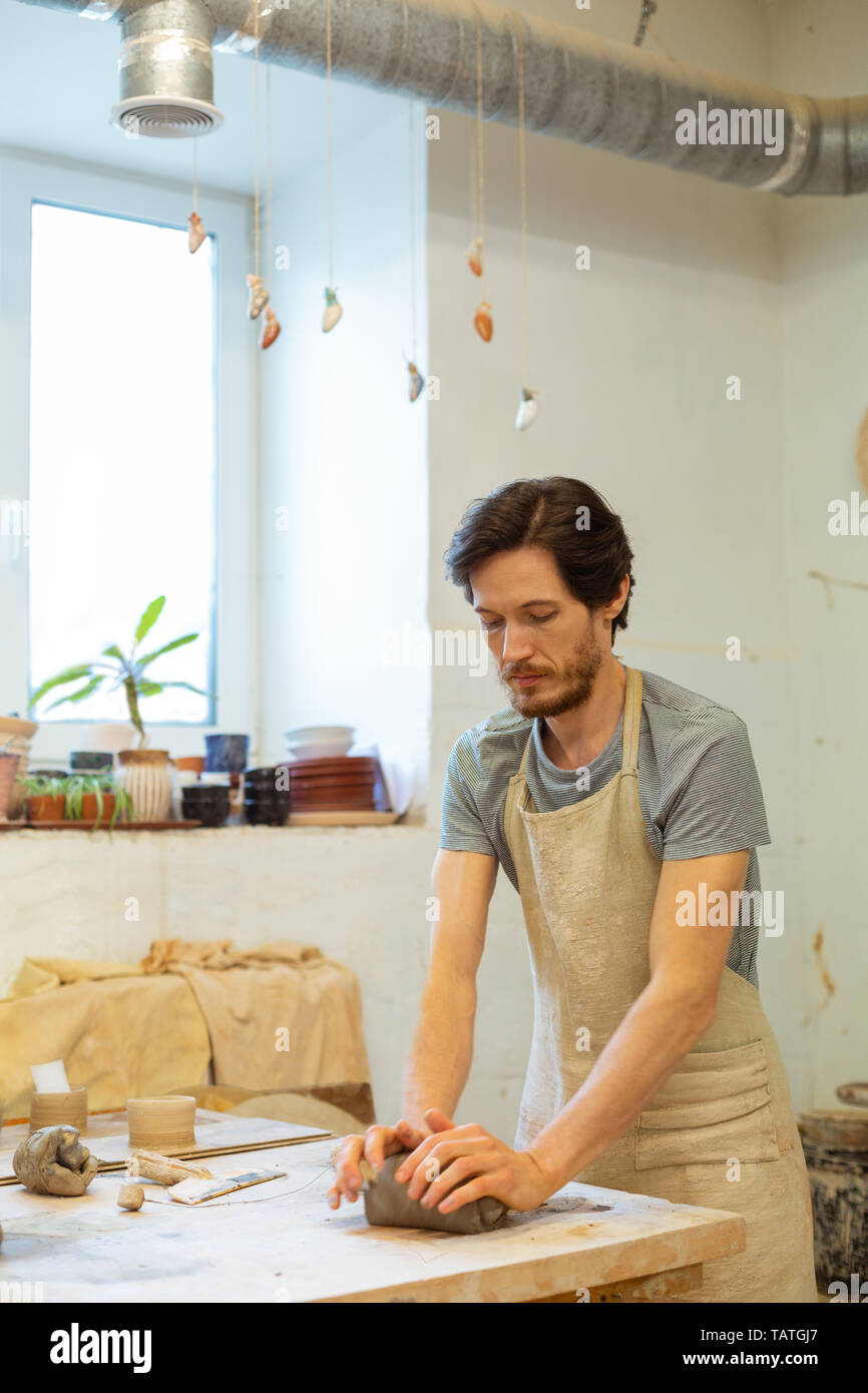 Beau atelier de poterie. Pacifique concentré brun frottant pièce d'argile humide tout en restant dans ce studio lumineux Banque D'Images