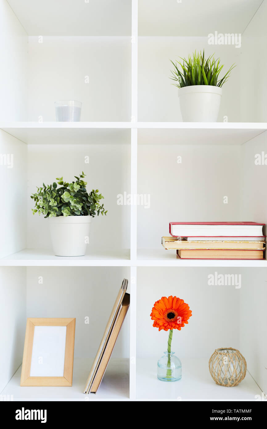 Plusieurs étagères de bureau carré blanc cabinet de plantes vertes en pots, cadre photo, livres, bougies et herbera orange Banque D'Images