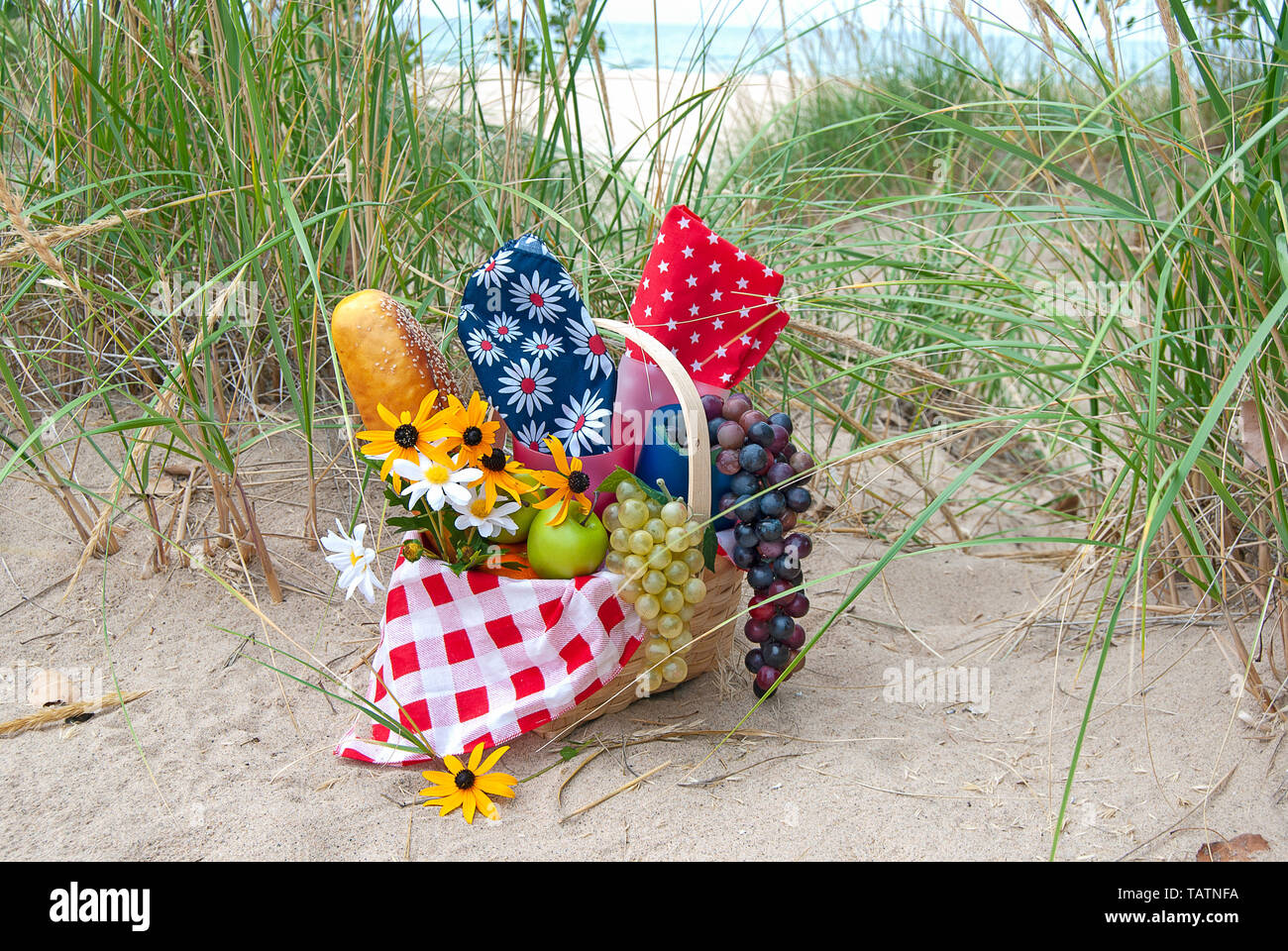 Marguerites d'été en panier pique-nique en bois rempli de fruits et de pain dans le sable de la plage et de l'herbe Banque D'Images