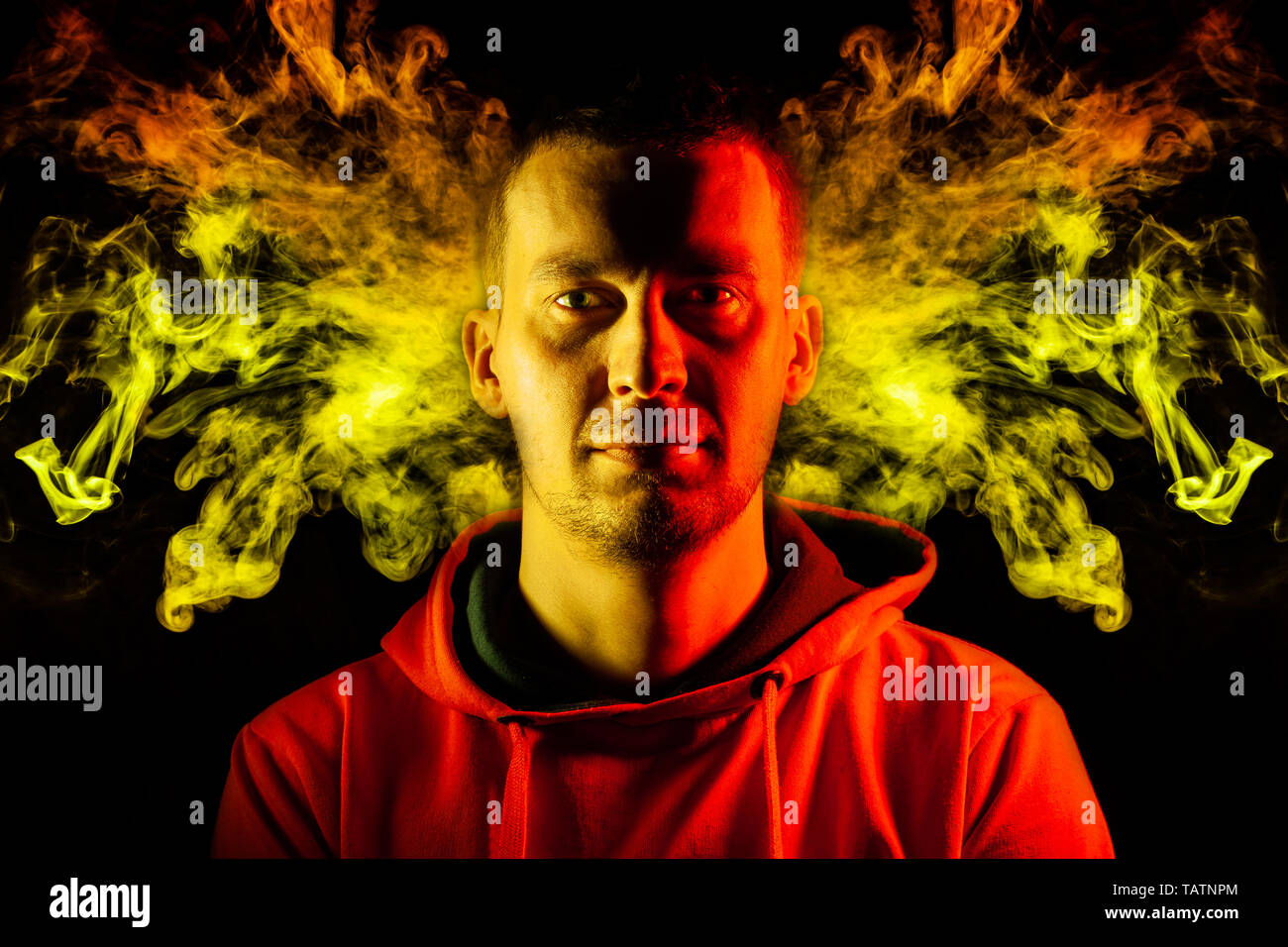 Un adulte guy est hâte in hoodie surlignés en jaune et rouge sur les côtés avec un sourire sur un fond noir motif isolé avec de colo Banque D'Images