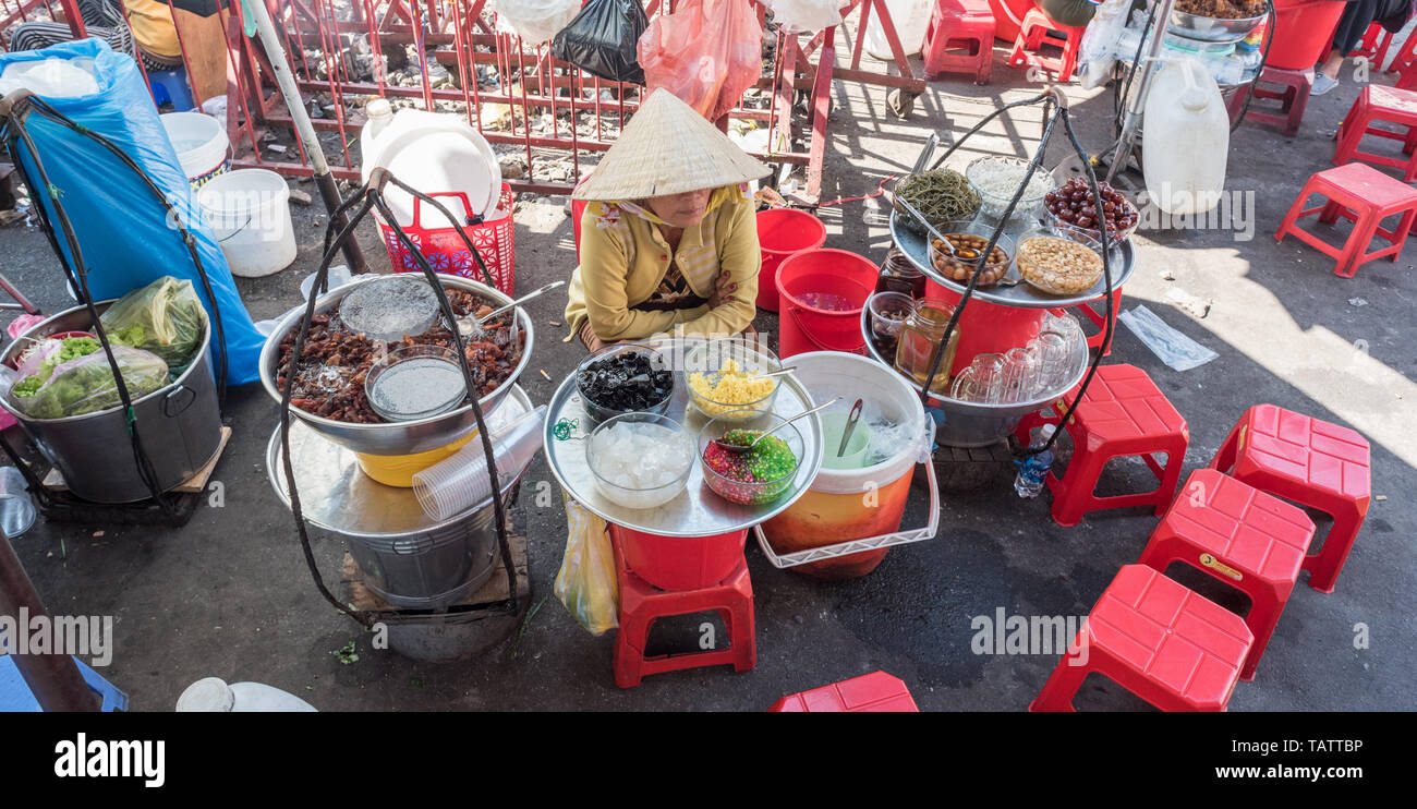 Ho Chi Minh Ville, Vietnam : un vendeur est assis par des plaques avec des ingrédients pour sam bo Luong, un froid Soupe sucrée (plat d'origine chinoise) marché Binh Tay Cho. Banque D'Images