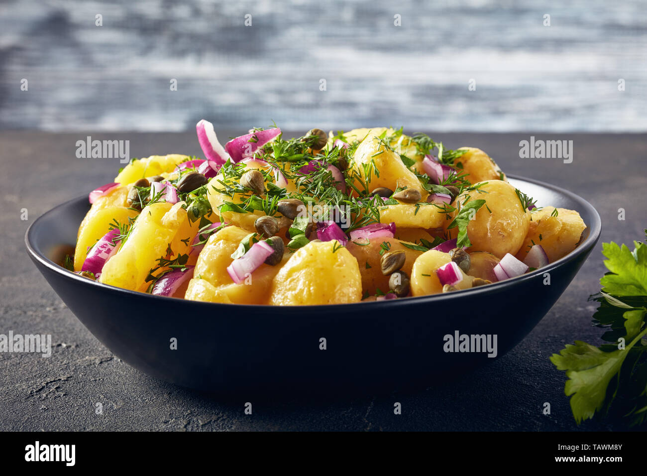 Close-up of salé salade de pommes de terre allemande avec l'oignon rouge, les câpres, les verts et la moutarde de vinaigre dans un bol noir sur une table, une vue d'abov Banque D'Images