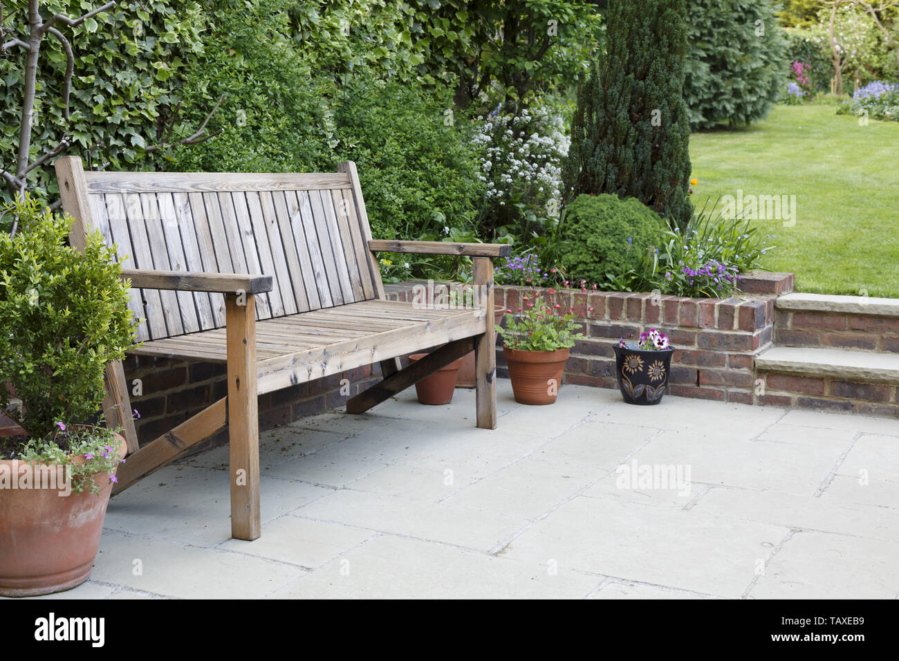 Retour en jardin avec une terrasse dallée et banc en bois traditionnel Banque D'Images