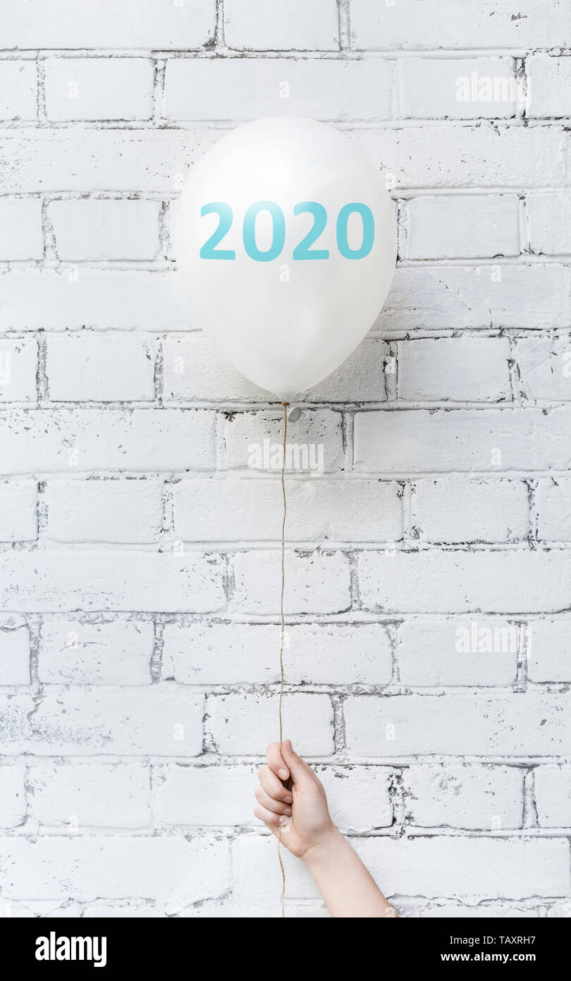 Woman hand holding 2020 ballon sur le mur de briques blanches Banque D'Images