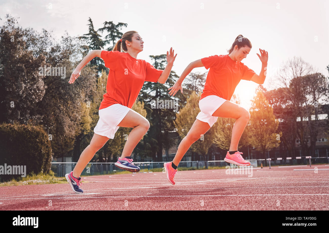 Athletic filles exécutant sur la concurrence - Les jeunes femmes chargées de séance d'entraînement sur la voie au coucher du soleil outdoor Banque D'Images