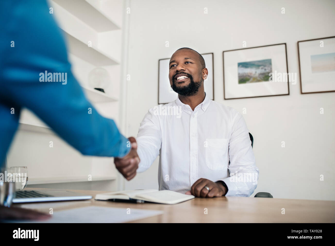 Smiling African American manager serrant la main d'un demandeur d'emploi à l'issue d'un entretien alors qu'il était assis à son bureau dans un bureau Banque D'Images
