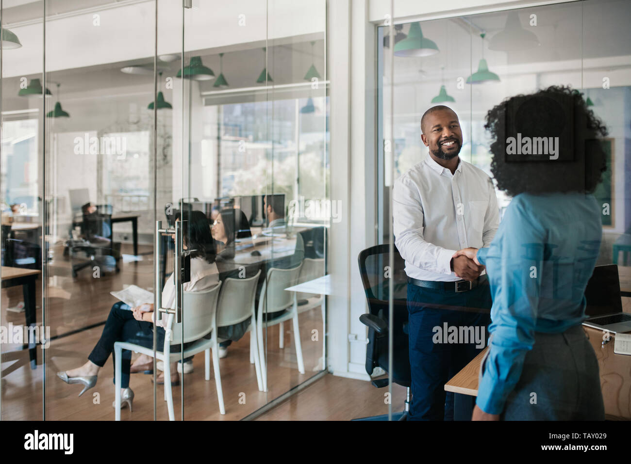 Smiling African American manager se tenant debout à l'intérieur de son bureau en serrant la main d'un nouvel employé à la suite d'une entrevue Banque D'Images