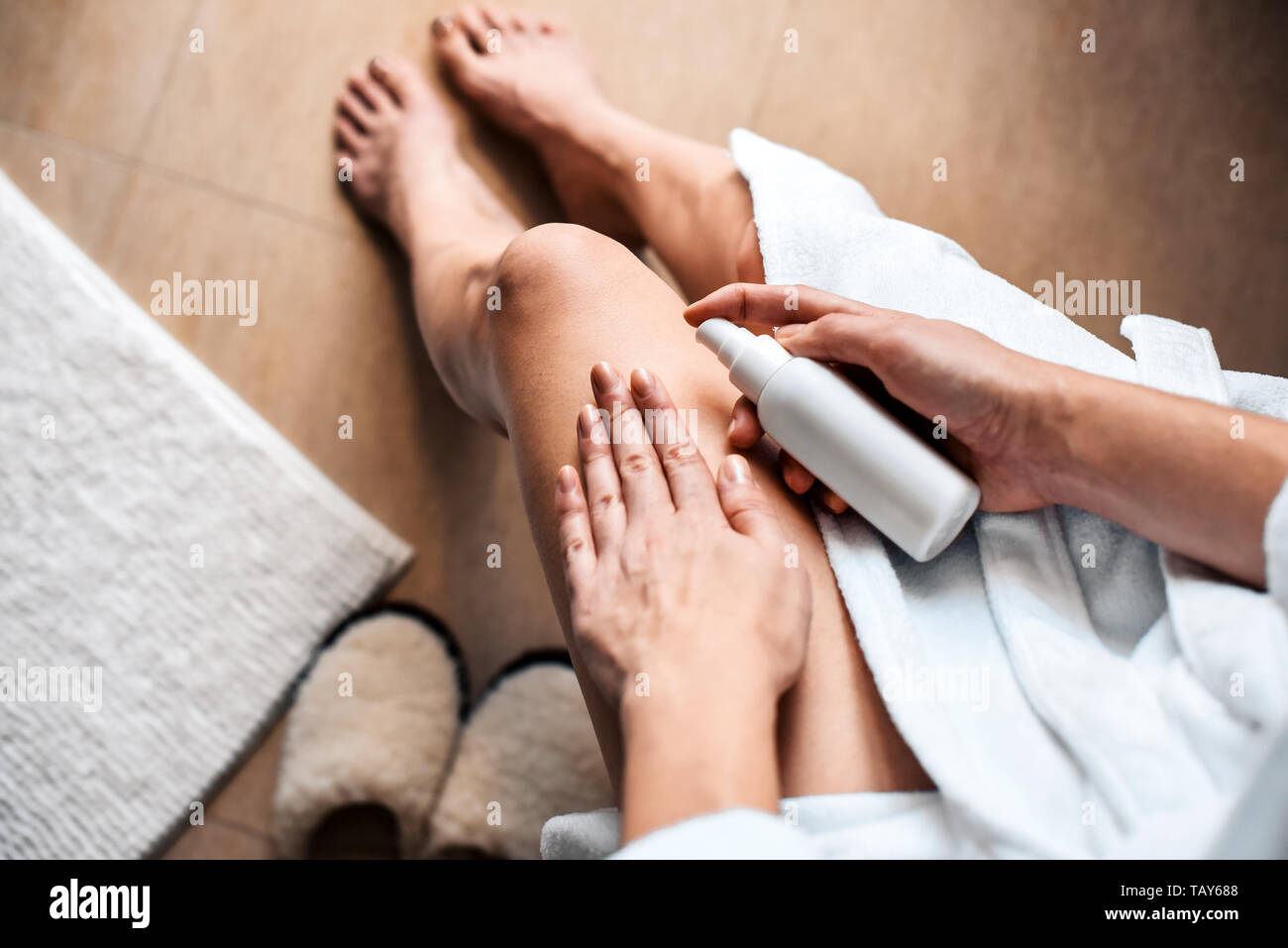 La jeune fille dans la salle de bains met la crème anti-cellulite, de sérum sur les jambes et le corps. Concept de soins du corps. Banque D'Images