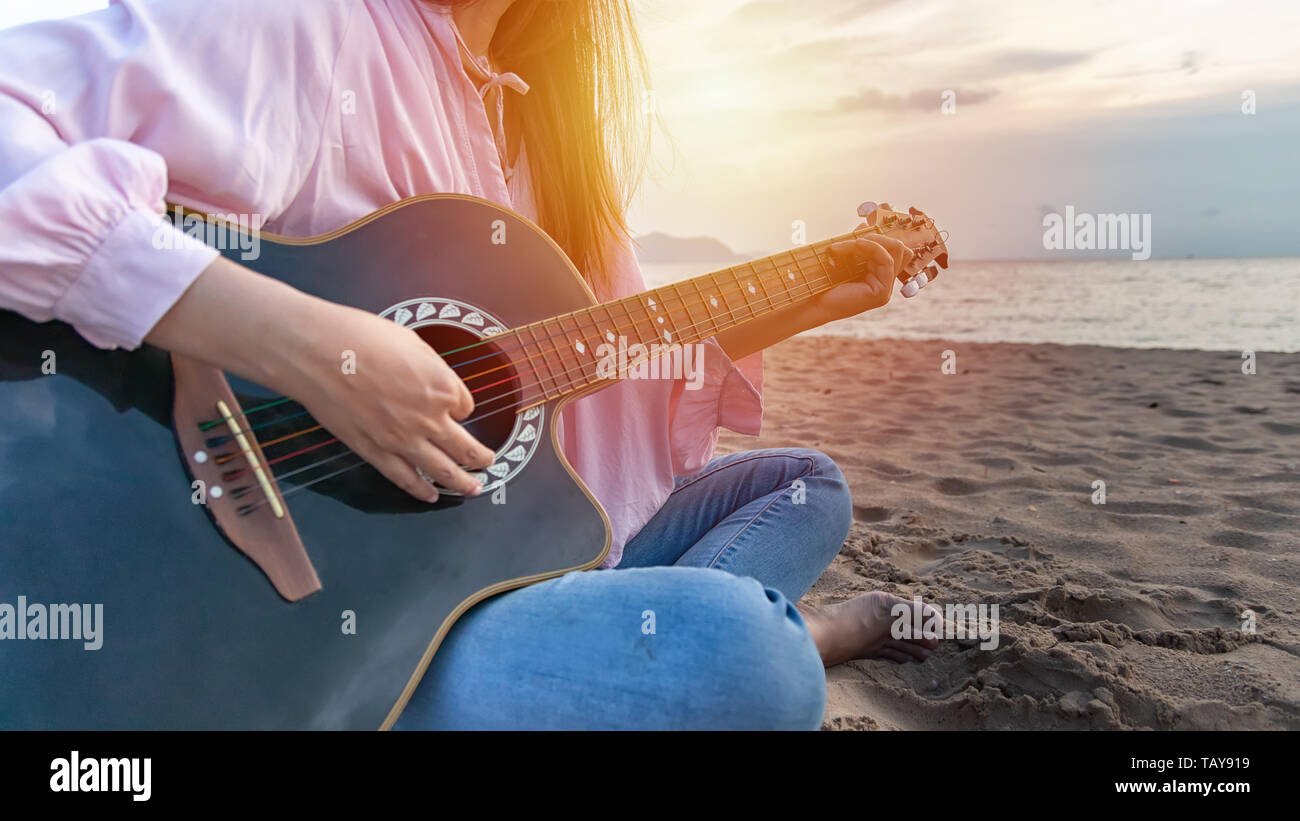 Woman's hands playing acoustic guitar chords, capture par le doigt sur la plage de sable à l'heure du coucher du soleil. lecture de musique concept Banque D'Images
