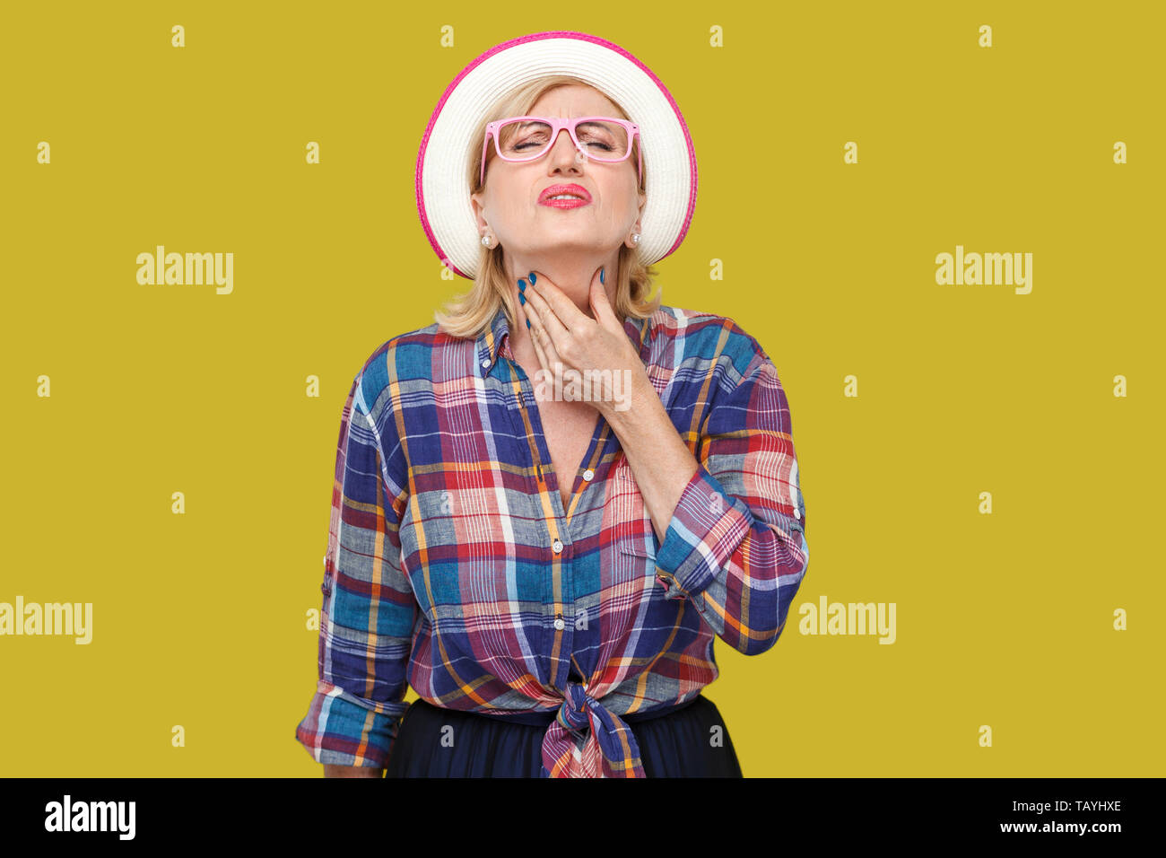 La maladie de gorge ou de la grippe. Portrait de femme mature élégant moderne malade dans un style décontracté avec chapeau et lunettes debout et tenant son cou douloureux Banque D'Images