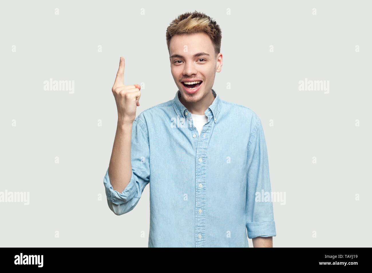 Portrait of handsome heureux heureux jeune homme en chemise bleu pâle, doigt de maintien permanent à appareil photo avec dents sourire, un visage surpris Banque D'Images