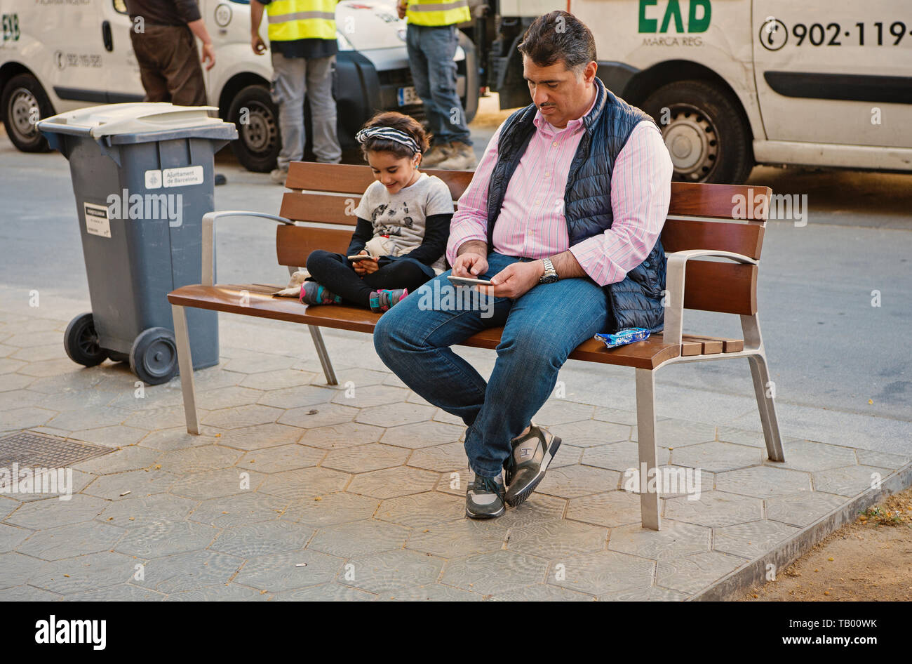 Barcelone, Espagne - 30 mars 2016 Père : l'homme et la petite fille recherchez dans les smartphones assis sur un banc on city street. La vie moderne. La nouvelle technologie. Vacances d'été et wanderlust. Banque D'Images