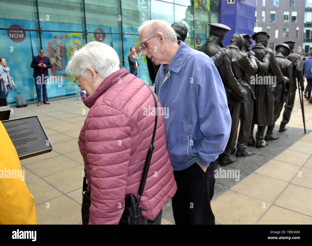 Les gens lisent l'avis décrivant la statue de sept soldats aveuglés à l'entrée de la gare Piccadilly de Manchester, Royaume-Uni Banque D'Images