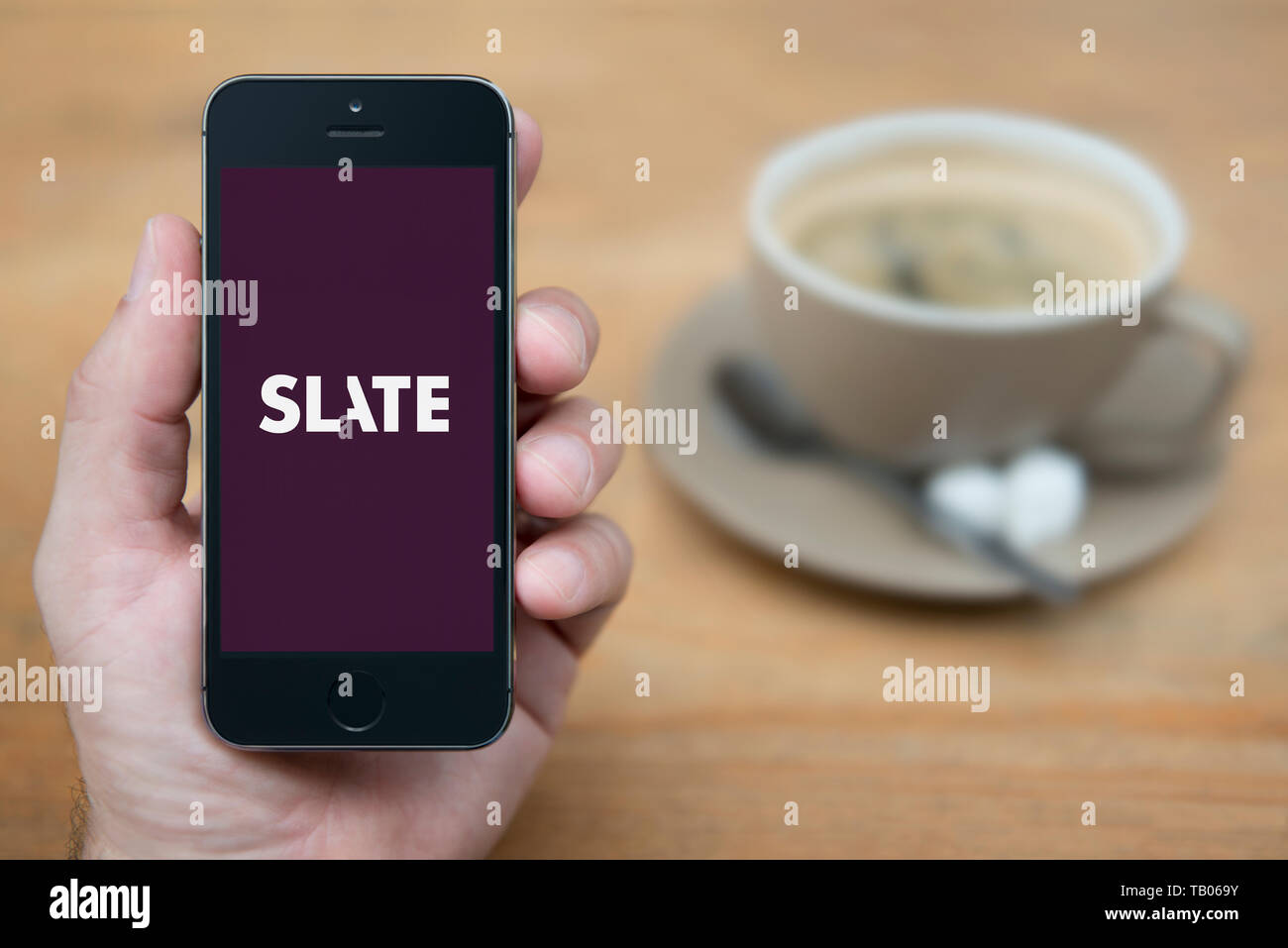 Un homme se penche sur son iPhone qui affiche le logo du magazine Slate (usage éditorial uniquement). Banque D'Images