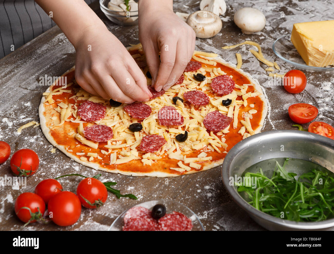 Woman Preparing Pizza, l'ajout de salami et d'Olives noires Banque D'Images