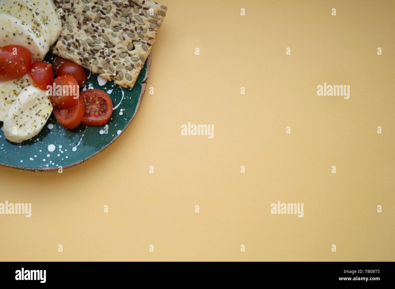 La mozzarella, tomates cerises et de basilic frais et des biscuits aux céréales sur la plaque en céramique fait main verte dans le coin supérieur gauche. Jaune lumière backg Banque D'Images