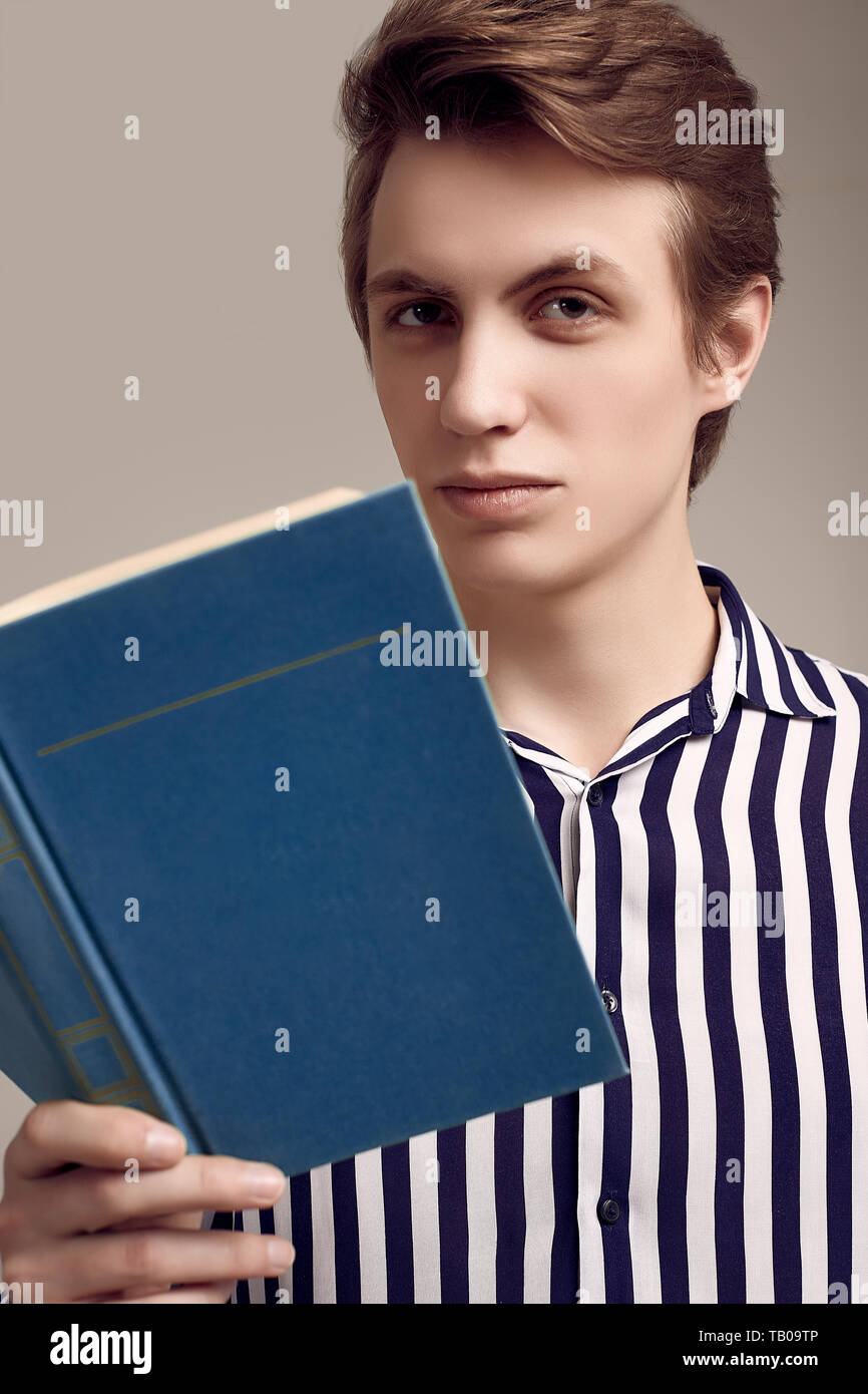 Fashion portrait de jeune homme séduisant en chemise rayée de la lecture d'un livre sur fond gris en studio Banque D'Images