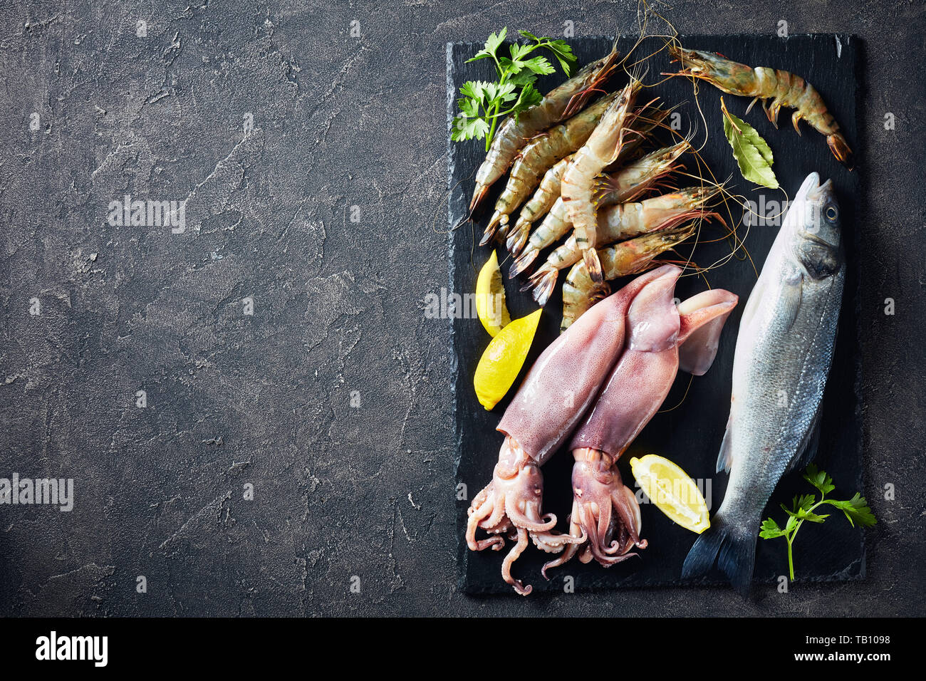 Basse mer entières, langoustines, calamars, tranches de citron, les épices et les herbes sur une plaque en ardoise sur une table, une vue de dessus, close-up, flatlay, co Banque D'Images