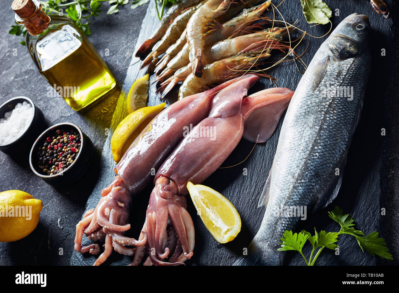 Loup de mer, crevettes, calmars, tranches de citron, les épices et les herbes sur une plaque en ardoise sur une table, une vue de dessus, close-up Banque D'Images
