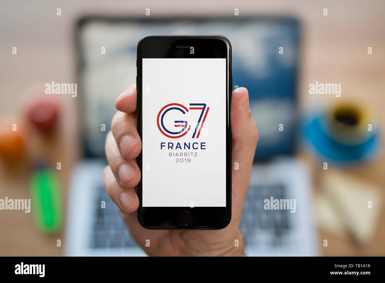 Un homme se penche sur son iPhone qui affiche le G7 France Biarritz logo du Sommet (usage éditorial uniquement). Banque D'Images