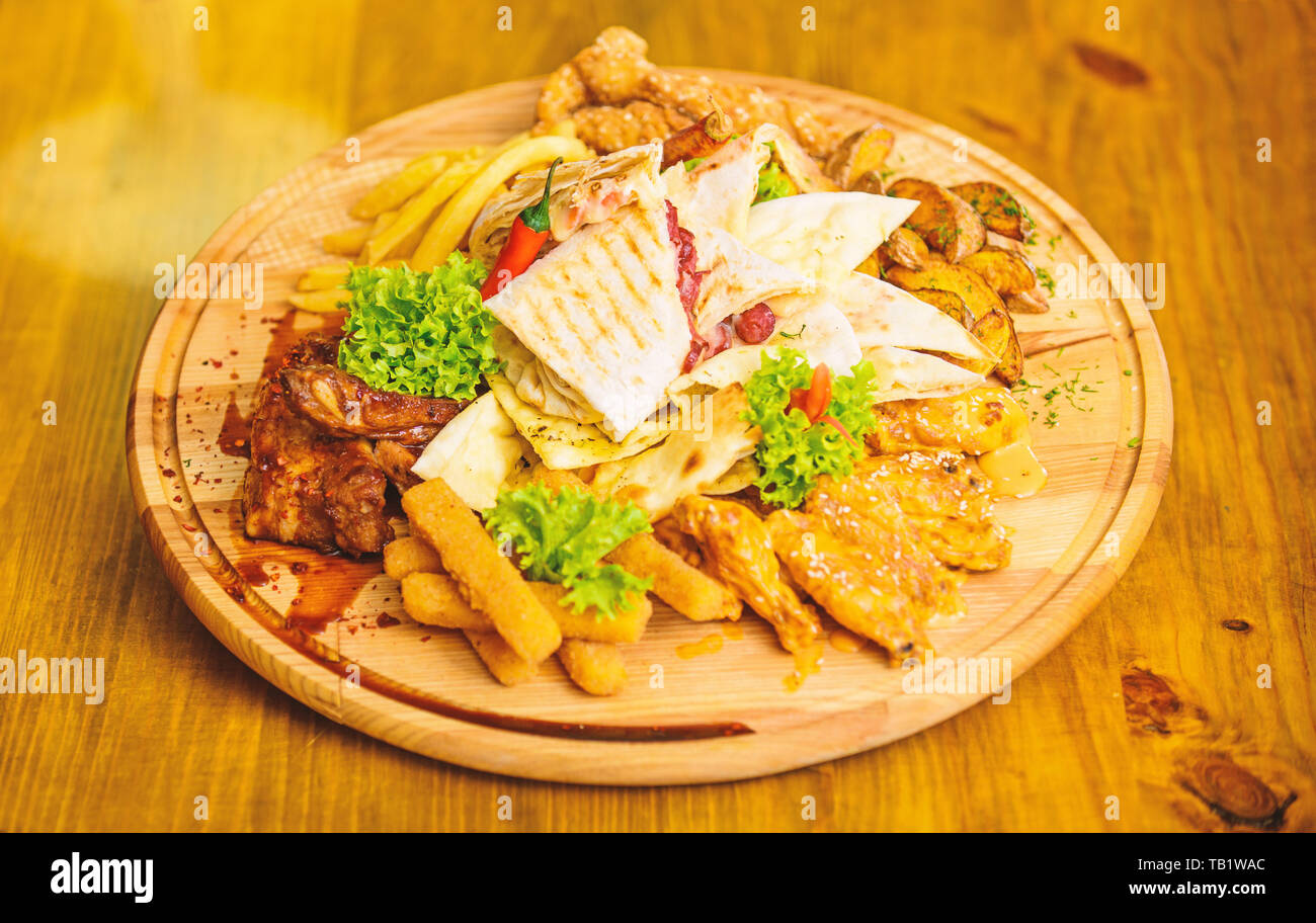 Menu snack-bar. De délicieux en-cas savoureux. Snack pour la bière. Les repas au restaurant. Planche de bois avec beaucoup de frites et bâtonnets de poisson viande burrito steak servi avec une salade. Calories élevé pour le groupe d'amis. Banque D'Images