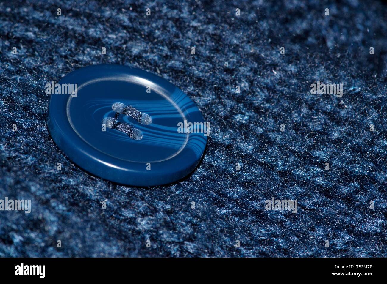 Macro image d'un bouton bleu en plastique cousue dans un cardigan bleu marine. Bouton est au centre et l'angle. Banque D'Images
