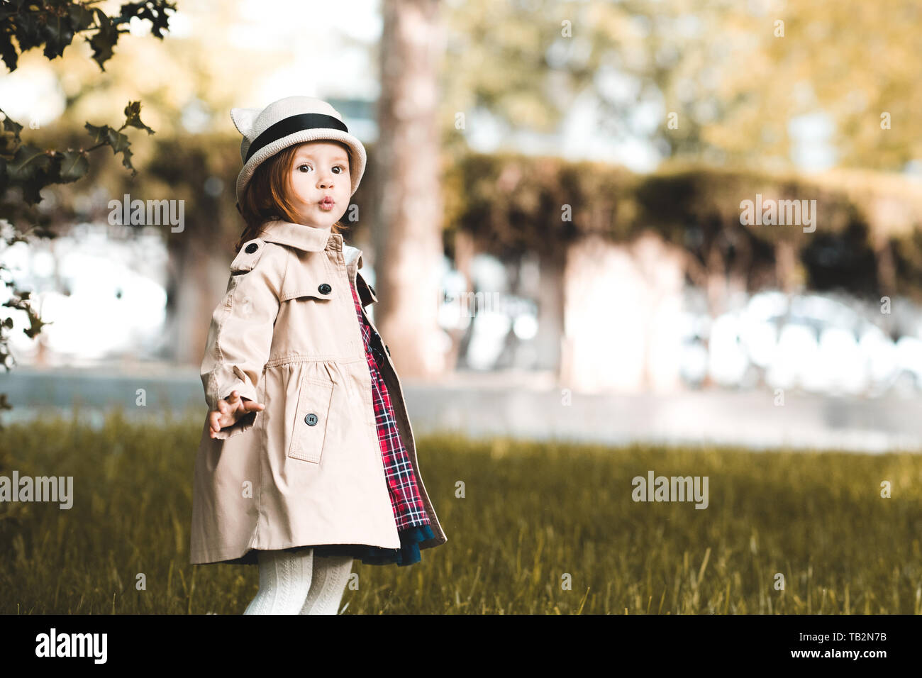 Funny baby girl 2-3 ans portant des tranchées élégant walking in park libre. L'enfance. Banque D'Images