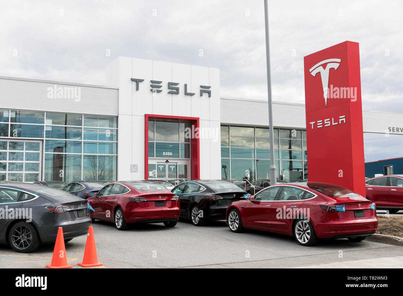 Un logo affiche à l'extérieur d'un concessionnaire de voiture Tesla avec le modèle 3 et le modèle S voitures dans le lot à Montréal, Québec, Canada, le 21 avril 2019. Banque D'Images