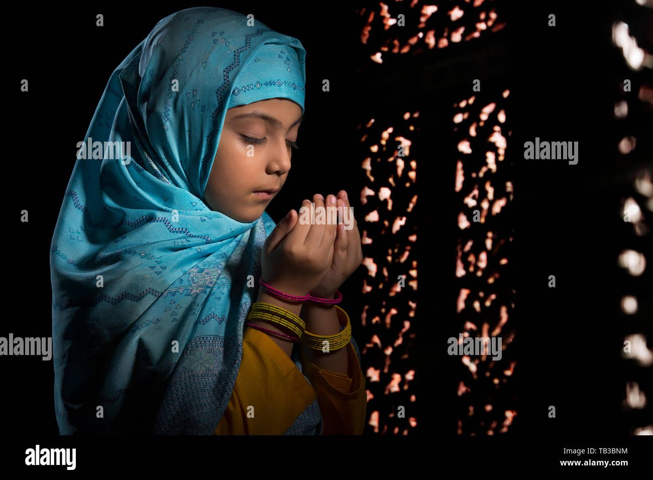 Jeune musulmane portant le hijab priant dans le noir avec les yeux fermé Banque D'Images