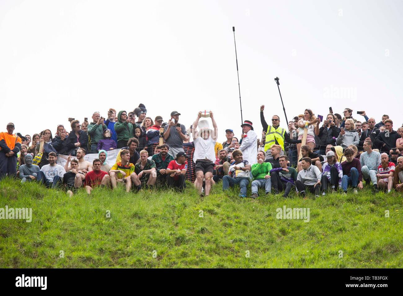 Un fromage est tenue en altitude avant la première course au cours de la banque annuelle de printemps maison de fromage-roulement événement à Cooper's Hill, près de Gloucester, mai 2019. Banque D'Images