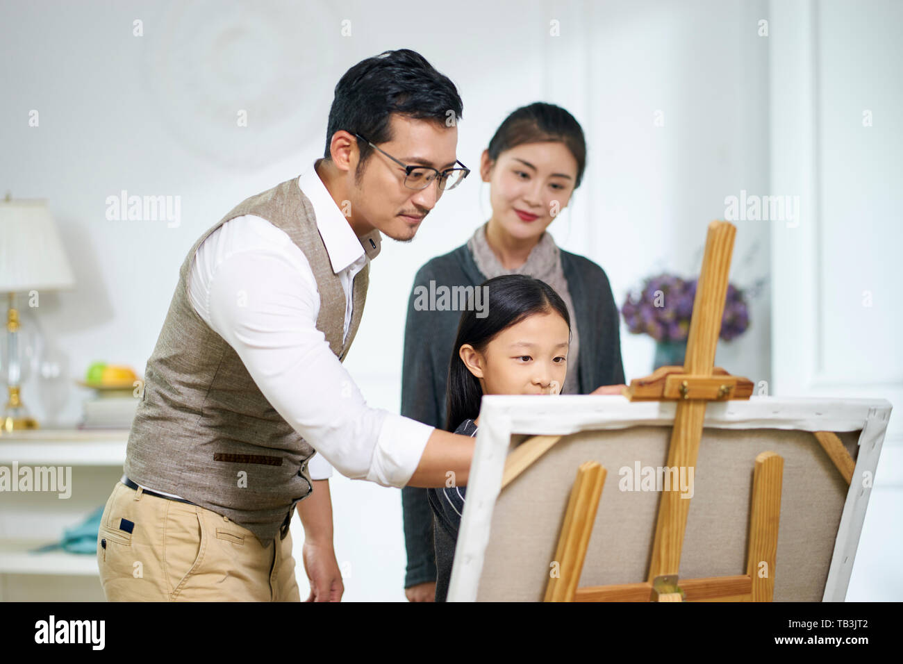 Petite fille asiatique faire une peinture obtenez de l'aide de père mère tout en regardant en arrière-plan Banque D'Images