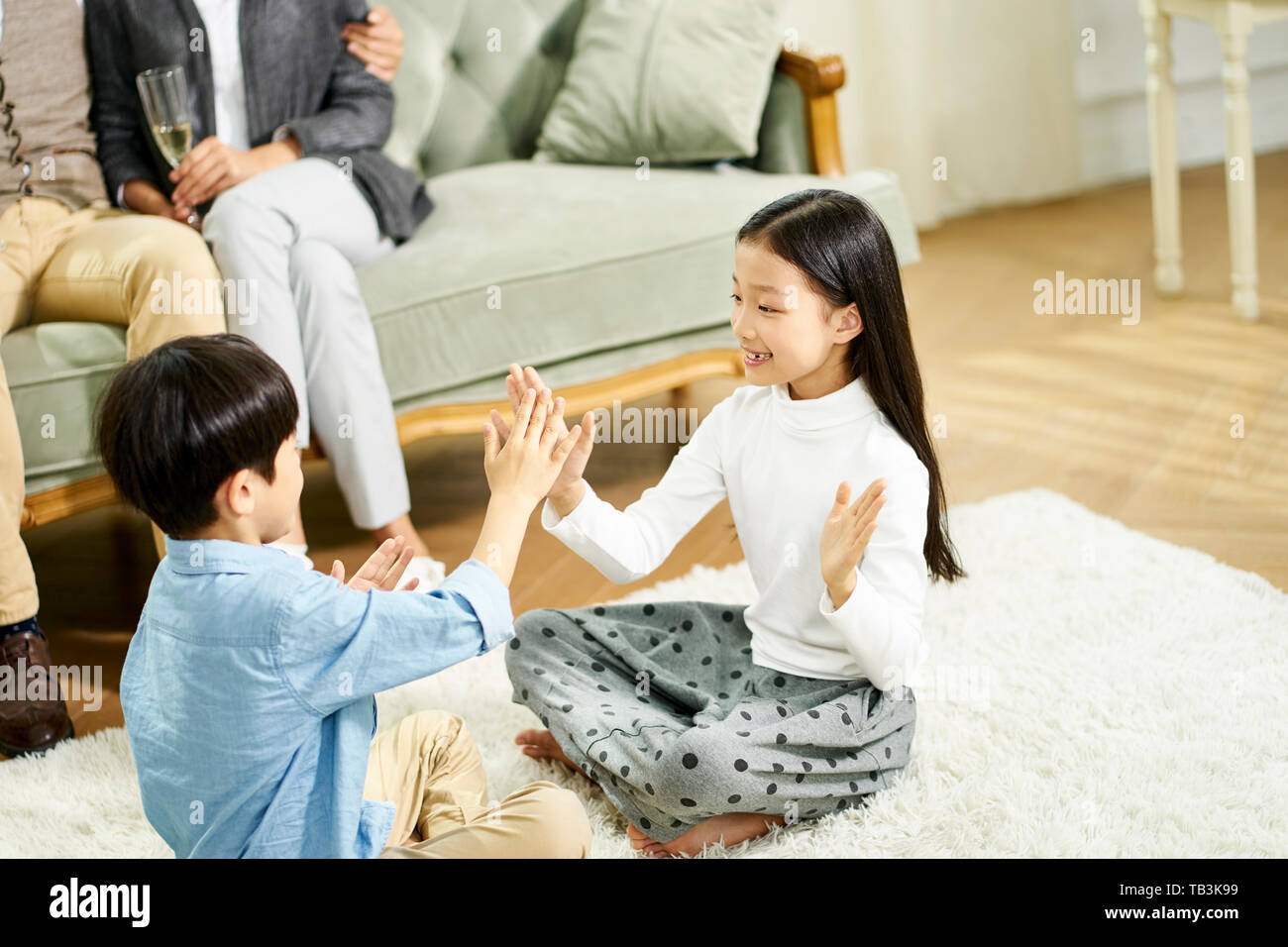 Deux enfants asiatiques mignon petit frère et sœur assis sur un tapis de jeu jouer avec parent assis sur un canapé à l'arrière-plan Banque D'Images