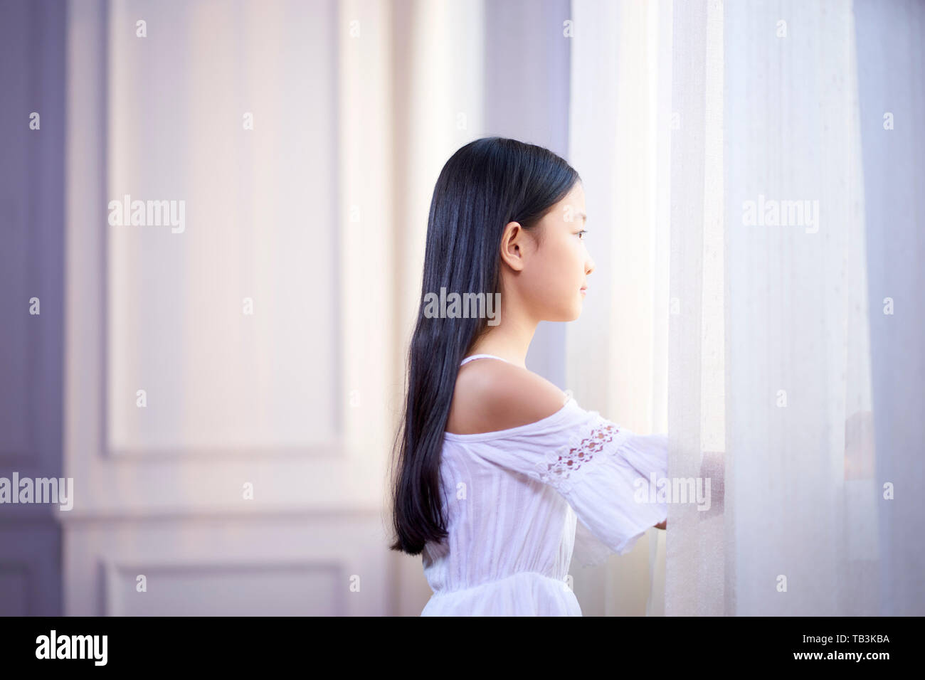 Belle petite fille asiatique avec de longs cheveux noirs à la fenêtre de sortie dans la chambre Banque D'Images