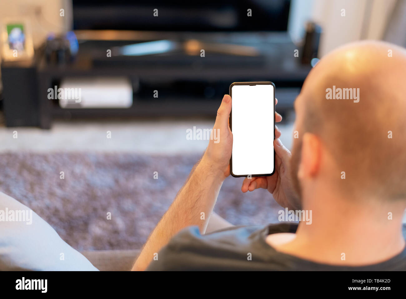 Homme de race blanche s'est assis dans la salle de séjour se penche sur son téléphone mobile Banque D'Images