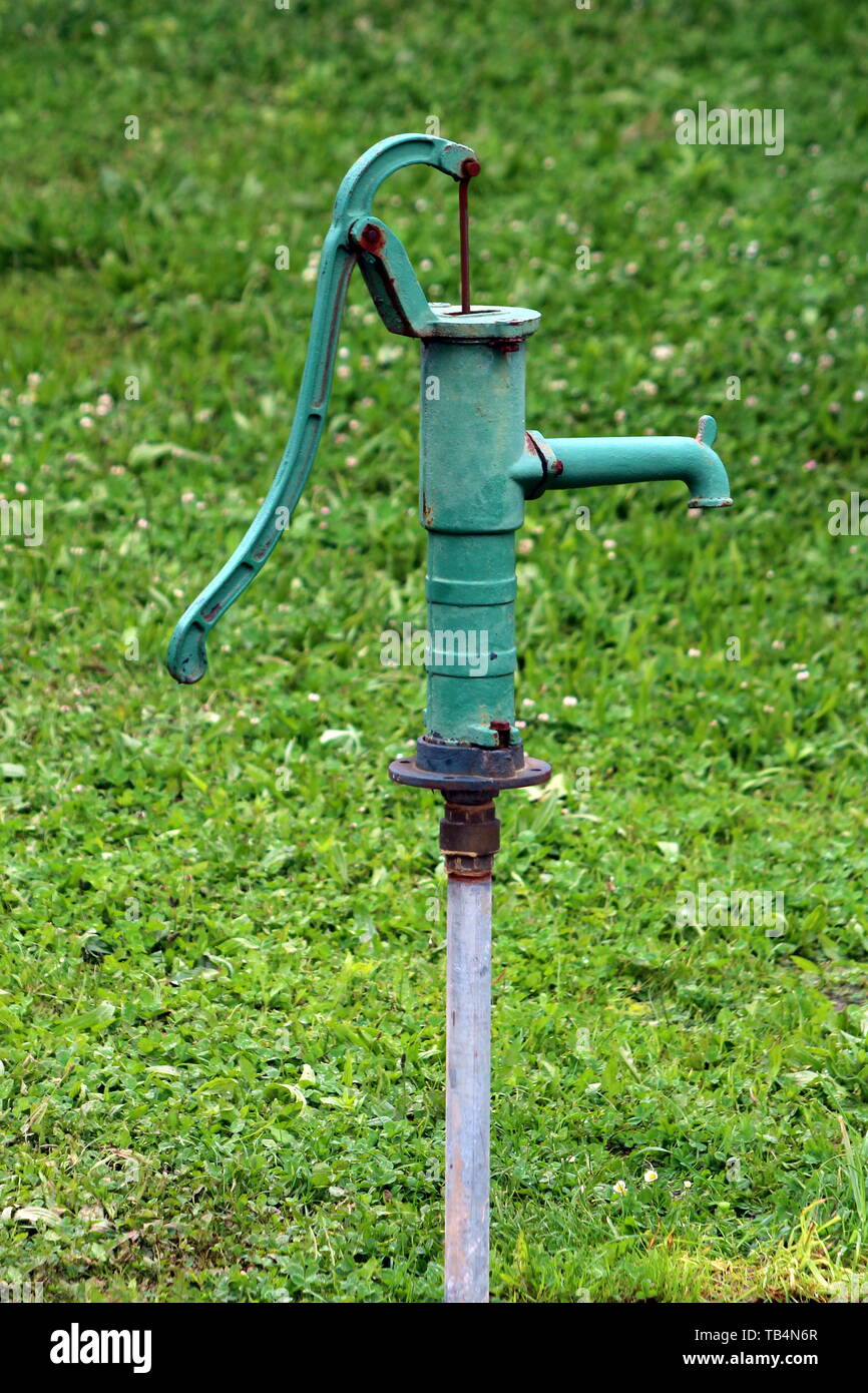 Vintage ancien en fer forgé vert rouillé part monté sur la pompe à eau tuyau métallique unique en jardin local entouré d'herbe non coupée sur le printemps chaud Banque D'Images
