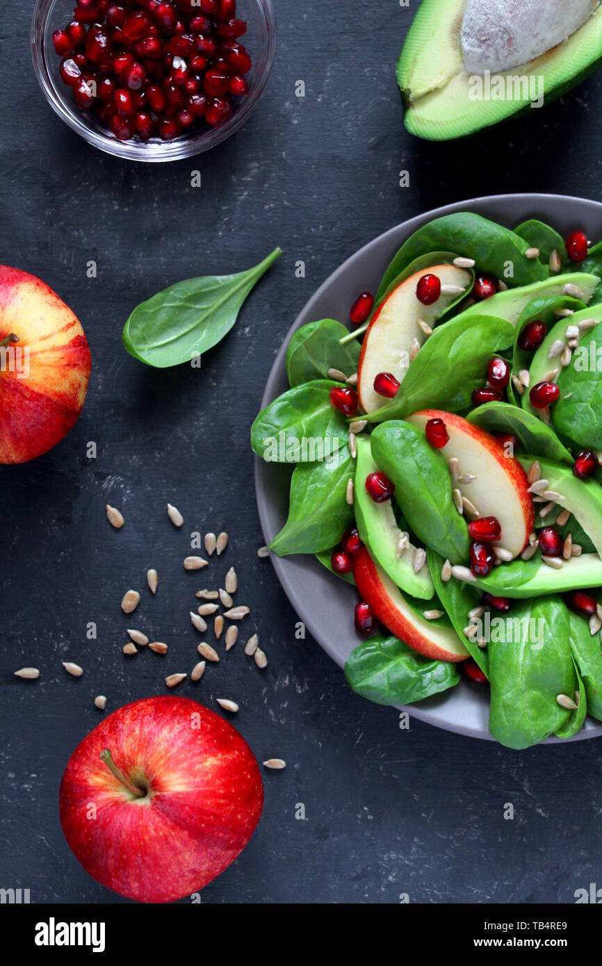 Avocat frais salade d'épinards, pommes, grenades et de tournesol sur fond sombre. Vue de dessus avec l'exemplaire de l'espace. Banque D'Images