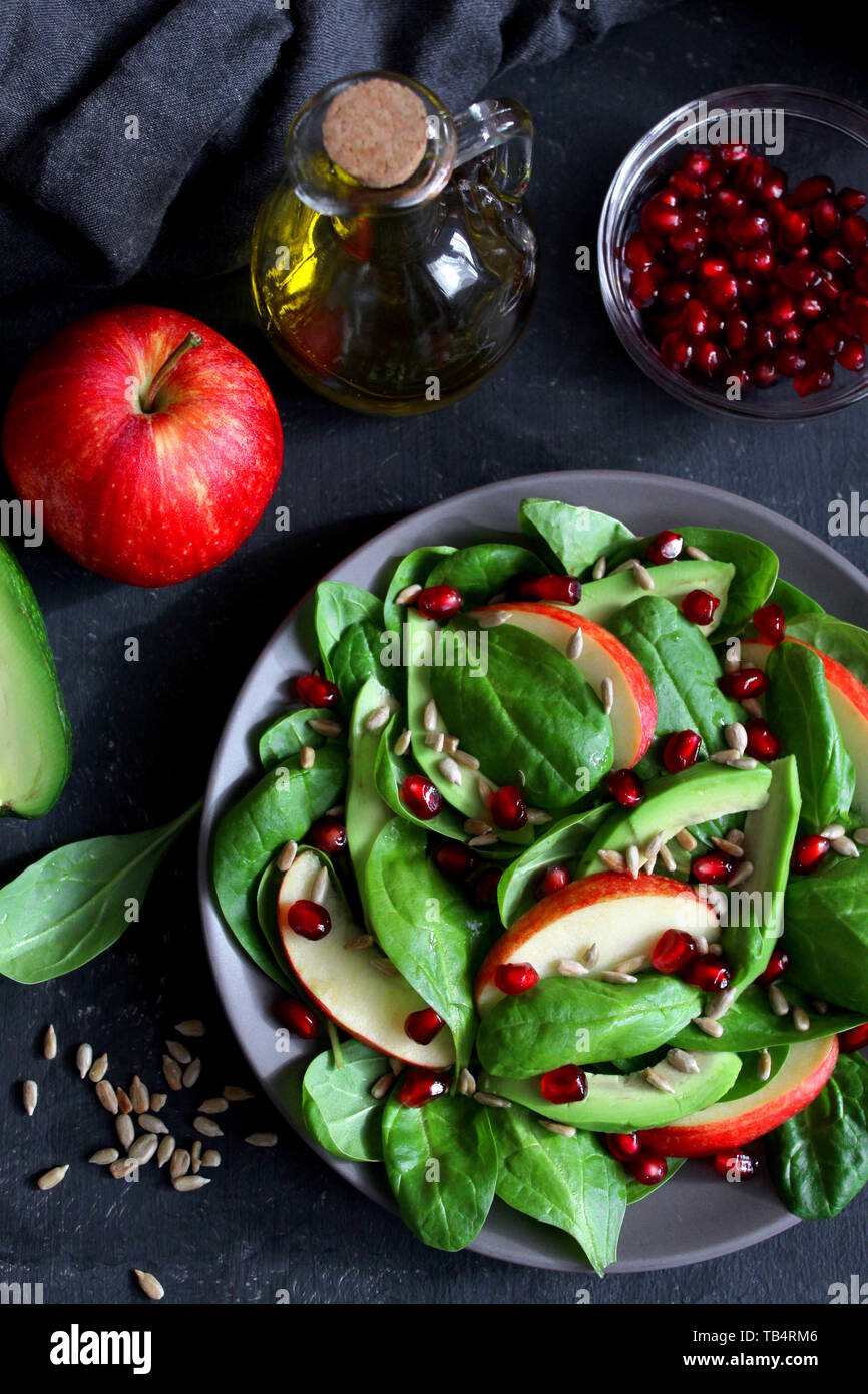 Avocat frais salade d'épinards, pommes, grenades et de tournesol sur fond sombre. Vue de dessus avec l'exemplaire de l'espace. Banque D'Images